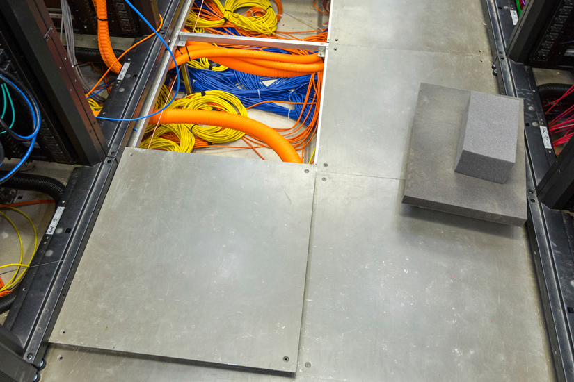 A single access opened showing various cables running under the floor