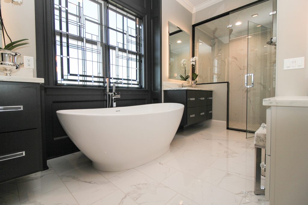 Bathroom with white tile floor, large white bathtub, and black cabinets