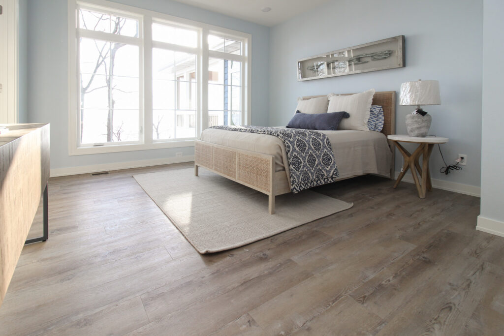 beige hardwood flooring in a light blue bedroom with beige area rug and beadspread