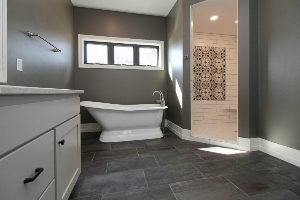 gray bathroom with black tiled floors, white tile shower and white bathtub